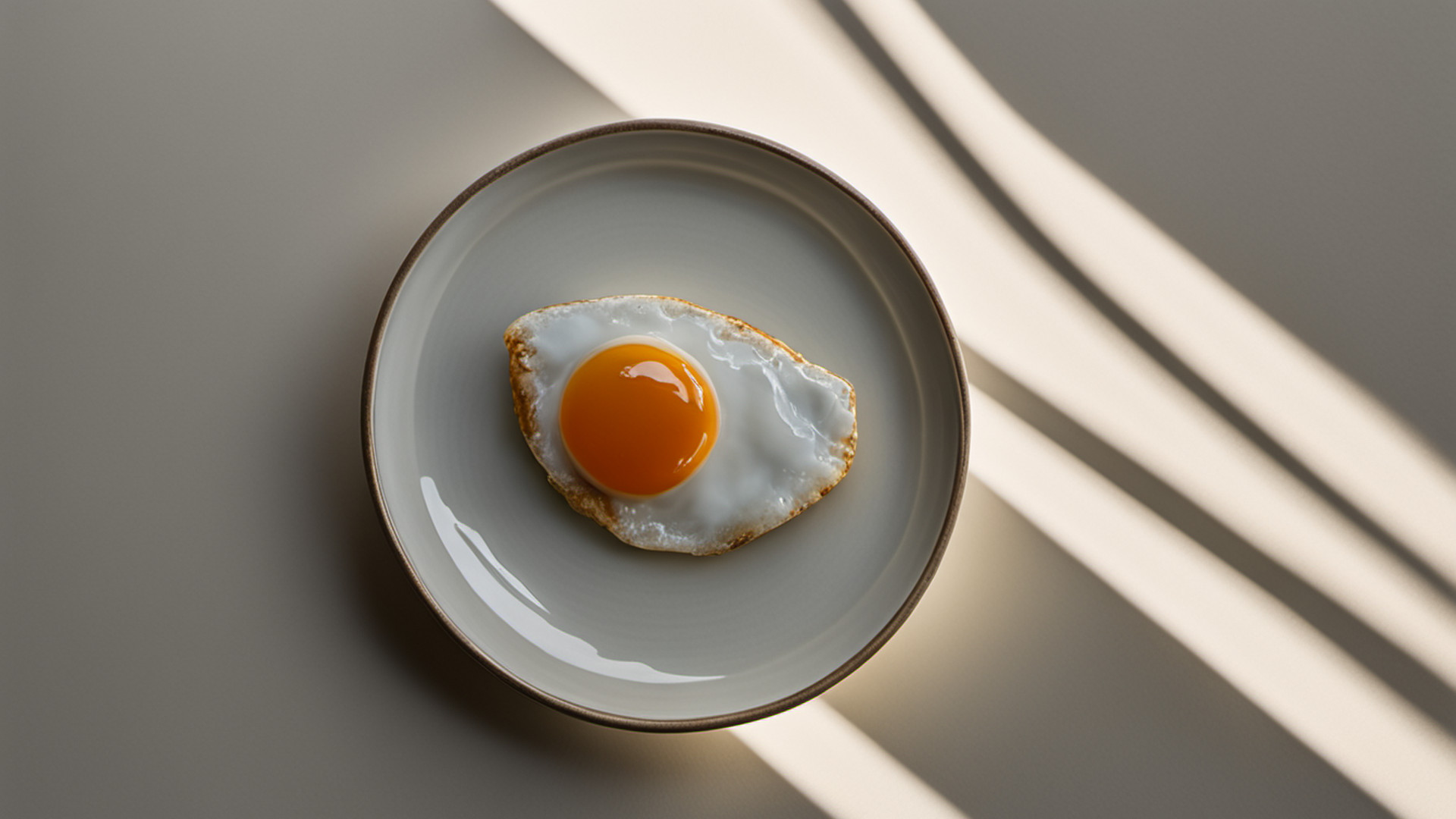 Generated plain fried egg on a plain plate representing the published eggs pairing; frying is not source-specified, and this is not a real product, ingredient, or premises photo